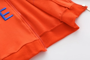 Detail eines orangefarbenen Kinder-Hoodies mit blauem E-Stick und goldenem Reißverschluss