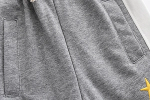 Detail of grey joggers featuring white side stripes and a yellow star embroidery