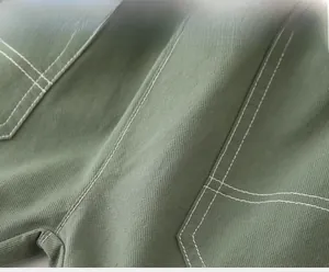 Gros plan du tissu sergé vert militaire avec surpiqûres blanches sur la poche