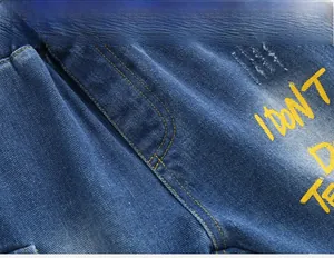 Macro detail of blue denim fabric with yellow stitching and graffiti lettering design