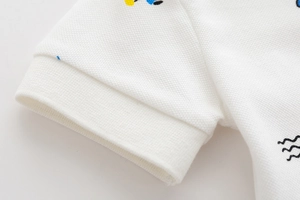Dettaglio macro della manica della polo bianca in piqué con stampe a cartoni animati
