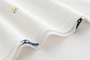 Dettaglio del tessuto piqué di cotone bianco con ricamo SURF e cucitura a doppio ago