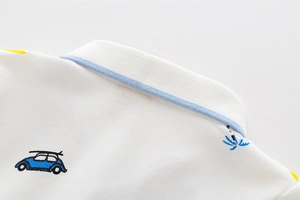 Dettaglio del colletto in cotone bianco con ricamo estivo e bordo blu a contrasto