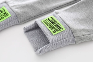 Macro shot of ribbed cuffs on gray cotton kids joggers with a neon green woven label