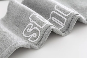 Close-up detail of grey knitted fabric with white block letter print on kids' joggers