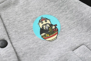 Detailed view of grey fleece jacket featuring cartoon elder embroidery and snap button