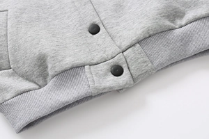 Detail of grey fleece sweatshirt ribbed hem with black snap buttons and knit texture