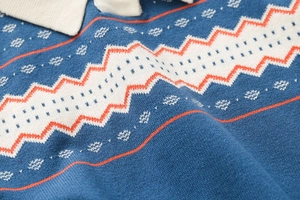 Dettaglio ravvicinato di maglione in maglia blu con motivi a onde arancio e texture a cuore