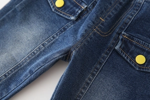 Détail d'un jean pour enfant avec délavage foncé, double surpiqûre et bouton jaune