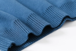 Dettaglio della trama a coste blu ciano sul polsino del maglione lavorato a maglia