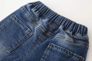 Détail de la taille élastique et des surpiqûres orange sur jean bleu pour enfant