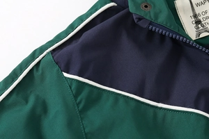 Detail view of children jacket featuring green color-blocking, zipper, and metal snap button