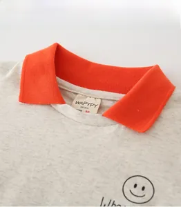 Détail du col d'un polo enfant en tricot gris avec bord-côte orange et motif smiley brodé