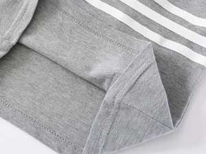 Detailed macro view of gray polo shirt hem featuring white triple-stripe athletic trim