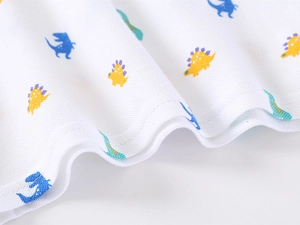 Detail of breathable white cotton pique fabric with colorful cartoon dinosaur prints