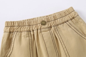 Detail of khaki cotton shorts featuring an elastic waistband and vintage bronze button
