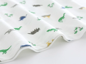 Detailed close-up of white soft knit fabric with colorful dinosaur and palm tree patterns