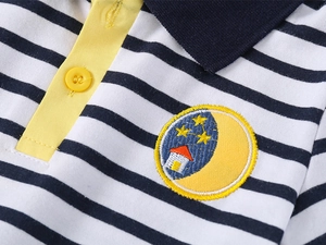Dettaglio polo a righe da bambino con abbottonatura gialla e stemma ricamato