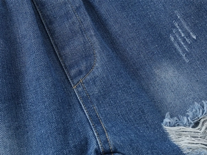 Macro view of blue denim fabric with orange stitching and distressed ripped details