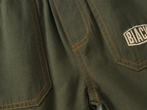Detail of army green cargo shorts showing orange contrast stitching and BLACK embroidery