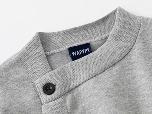 Dettaglio del maglione in maglia grigio chiaro con collo incrociato e bottone nero singolo