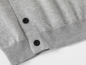 Dettaglio macro del cardigan grigio in maglia con bottoni neri e bordo a coste