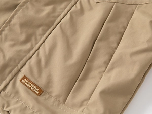 Detail of khaki quilted kids jacket showing vertical stitching and a brown leather patch