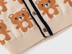 Detail view of beige knitted baby cardigan with brown bear patterns and wooden buttons