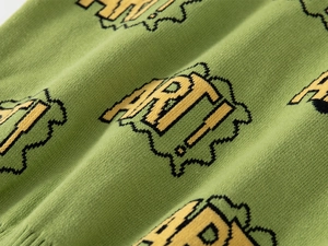 Detail of green knit sweater showing pixel-style ART pattern and ribbed hem texture