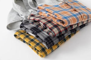 Folded boys plaid flannel shirts and grey hooded shirt in multiple colors with buttons