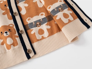 Detailed view of the cute teddy bear pattern and navy knit ribbing on an orange cardigan