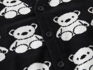 Macro detail of knit cardigan featuring black fabric with white bear pattern and buttons