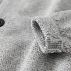 Dettaglio del cardigan in maglia grigia con polsini a costine e bottone nero raffinato