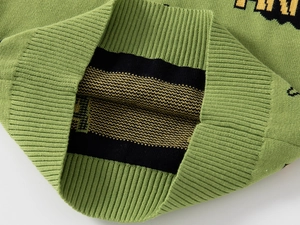 Close-up of green knit sweater showing ribbed cuffs and detailed jacquard letter pattern