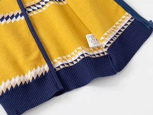 Détail d'un pull pour garçon montrant la maille jaune, le zip bleu et l'étiquette de taille 90