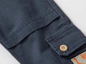 Détail de la poche cargo sur pantalon bleu marine pour enfants avec rabat et broderie orange