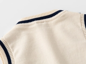 Dettaglio del gilet in maglia per bambini con scollo a V, righe blu navy e tessuto crema