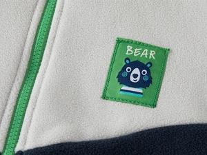 Close-up of kids fleece jacket showing zipper detail and blue bear patch embroidery
