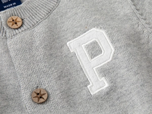 Détail d'un cardigan gris en maille avec boutons en bois étoilés et écusson blanc P
