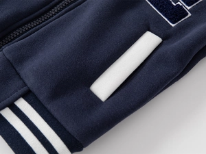 Detail of boys navy baseball jacket showing zipper, striped hem and textured letter embroidery