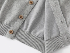 Détail d'un cardigan en maille grise avec boutons ronds en bois et gravures d'étoiles
