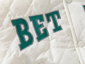 Close-up of diamond-quilted white jacket featuring green BET letter embroidery and matte buttons