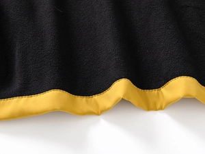 Détail de polaire noire avec bordure jaune et coutures précises sur une veste enfant