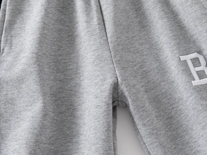 Detailed close-up of embroidered letter B on gray cotton children sports trousers