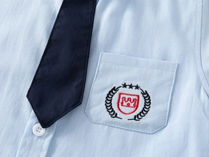 Detail showing high-quality embroidery on light blue shirt pocket with a navy tie