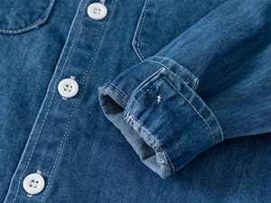 Dettaglio di camicia di jeans blu con bottoni bianchi e cuciture rinforzate