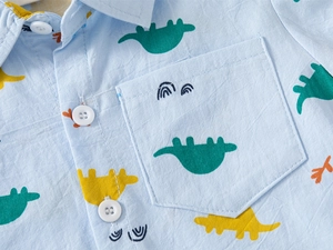 Détail d'une chemise enfant bleu clair avec imprimé dinosaure et petite poche frontale