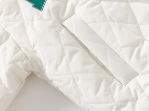 Macro detail of white diamond quilted fabric with green embroidered varsity letter