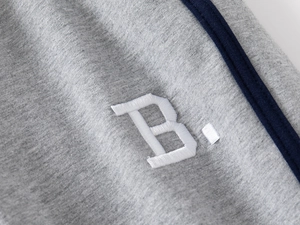 Detailed macro shot of grey kids joggers featuring blue side stripes and white B embroidery