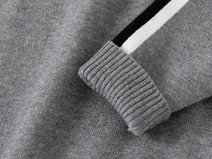 Détail du poignet d'un pull en tricot gris avec des bandes sportives noires et blanches